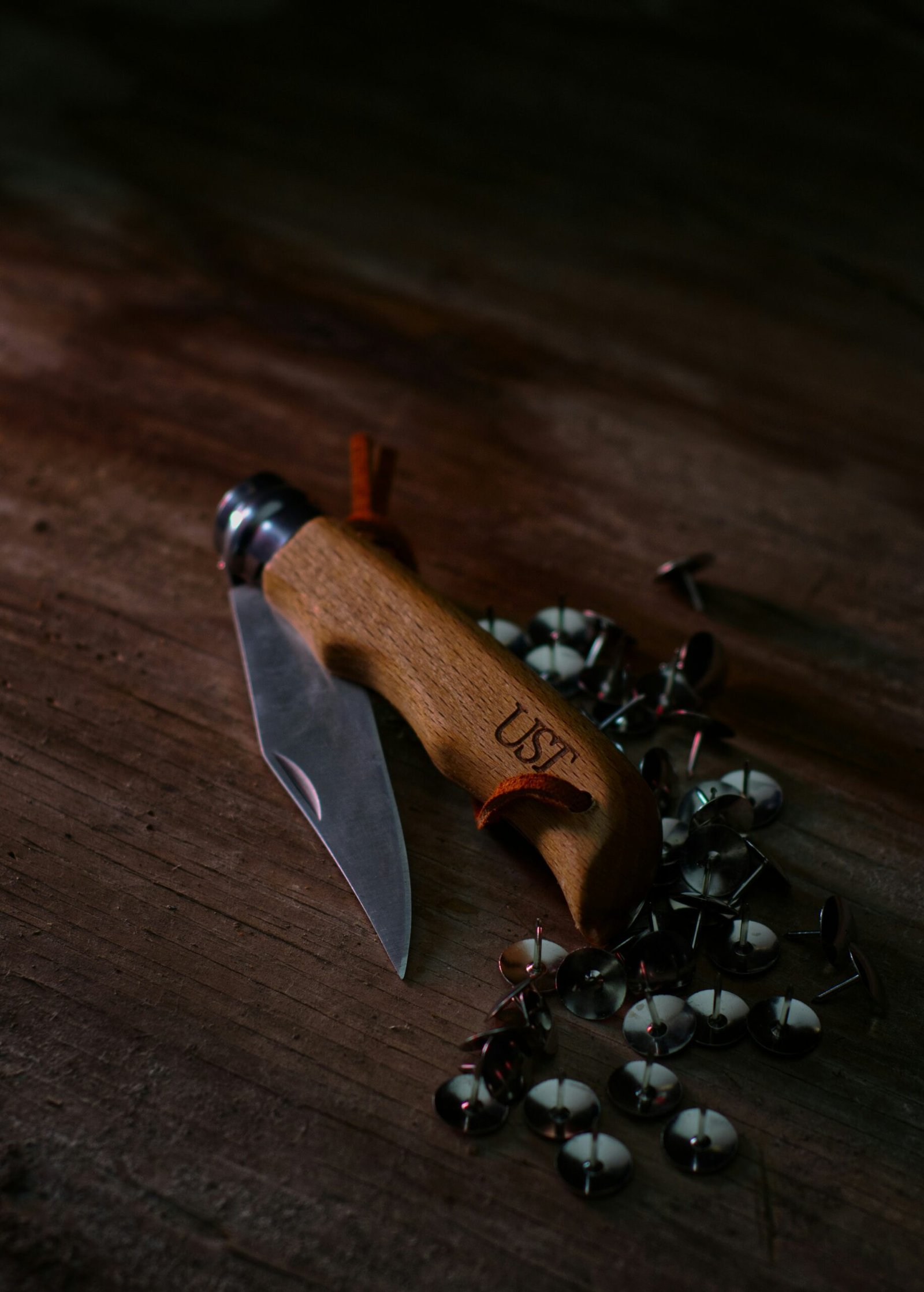A top-down view of a tactical folding knife resting on a dark, weathered log. The knife has a partially serrated silver blade and a handle made of polished wood with visible screws.